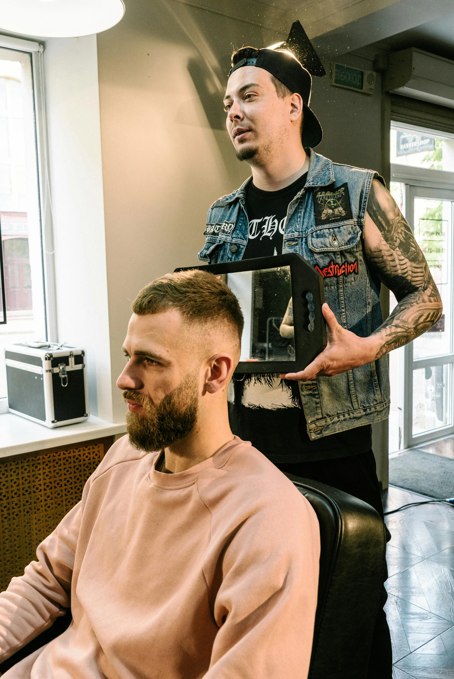 man getting a hair cut at barber shop with a man dressed in a jean vest