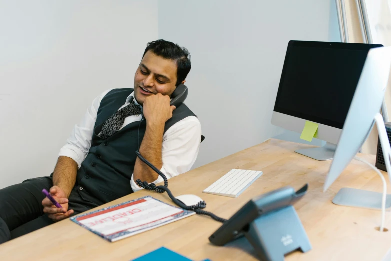 a man sitting at a desk with a phone up to his face