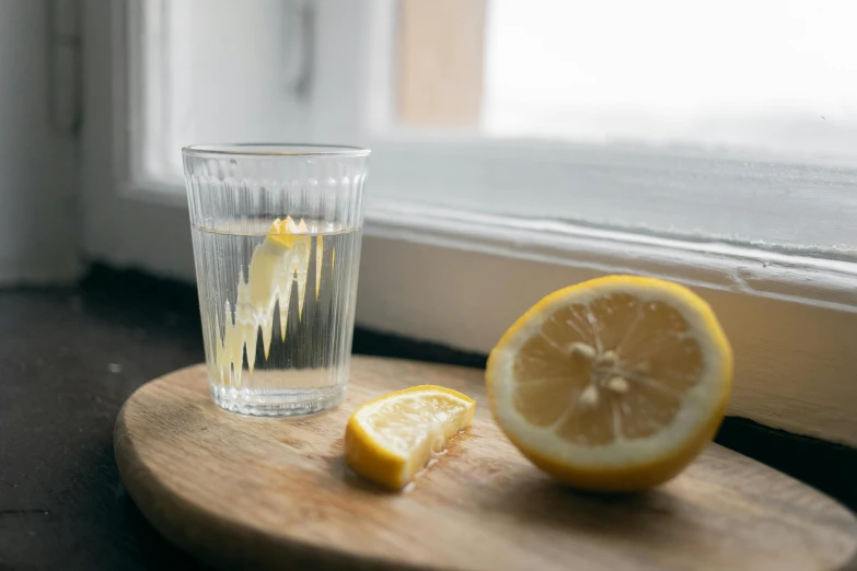 glass with liquid sitting on top of  board near lemon