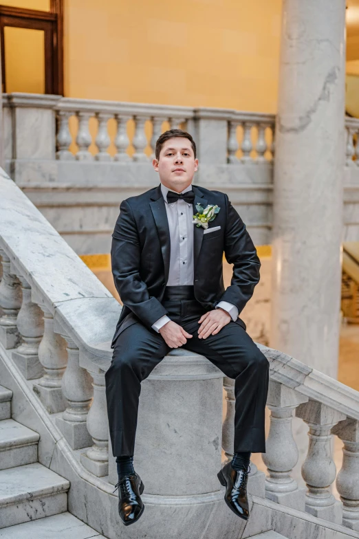 a young man in a tuxedo sits on a staircase