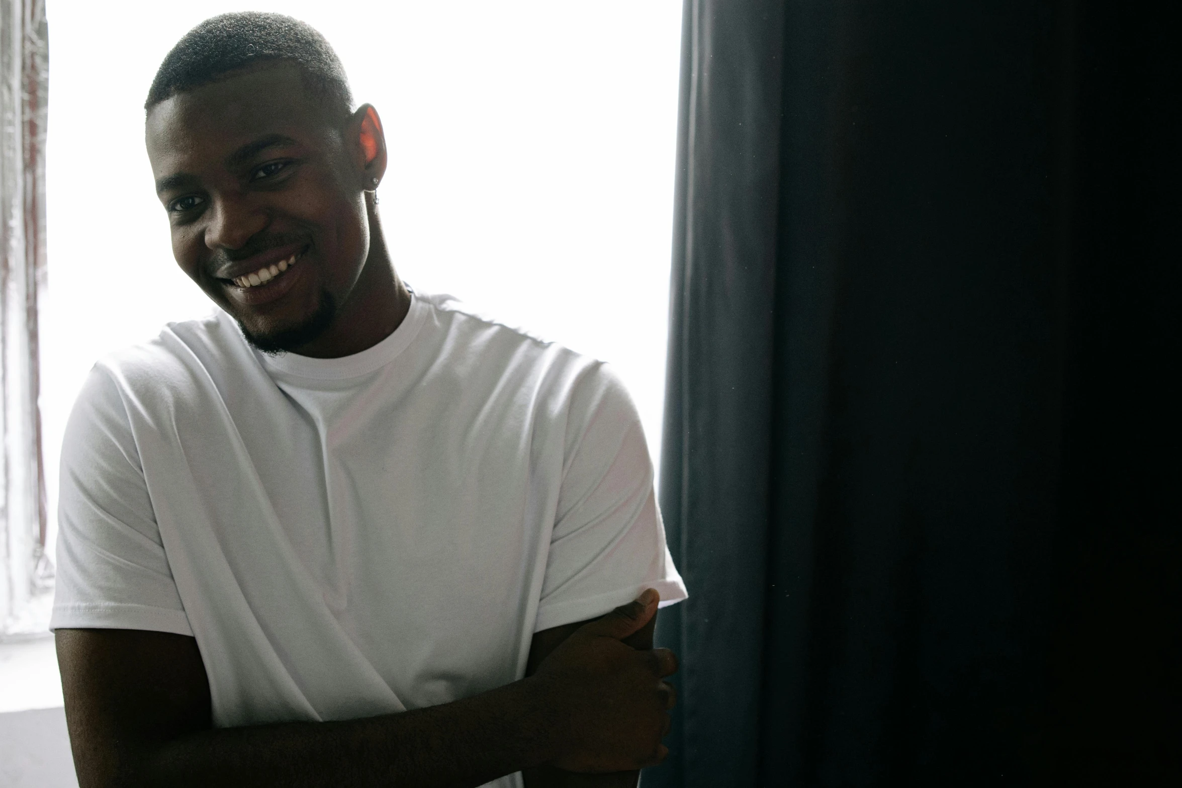 a black man is smiling and standing in front of a window