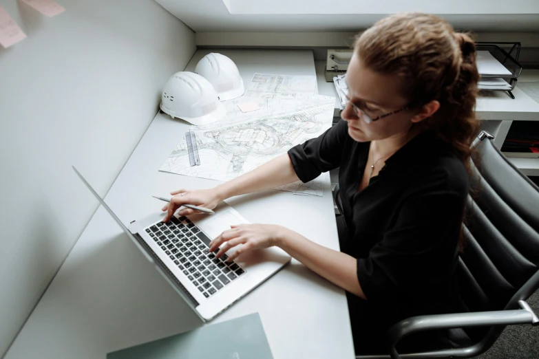 a woman with glasses is sitting at a desk using her laptop