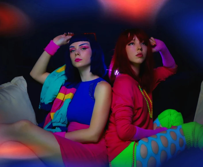 two young women sit on a couch wearing neon clothing