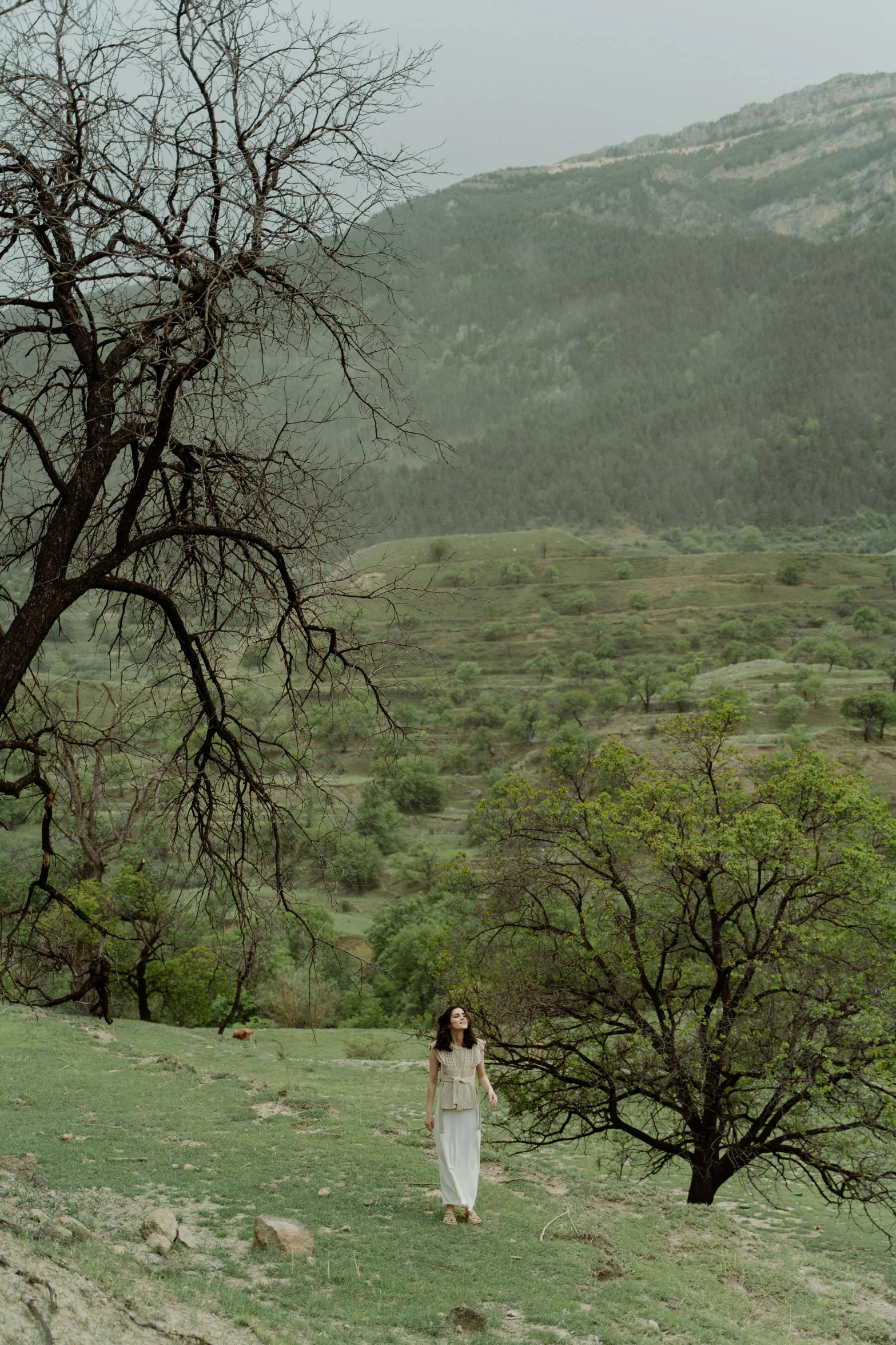 a woman in long white dress walking with trees in the background