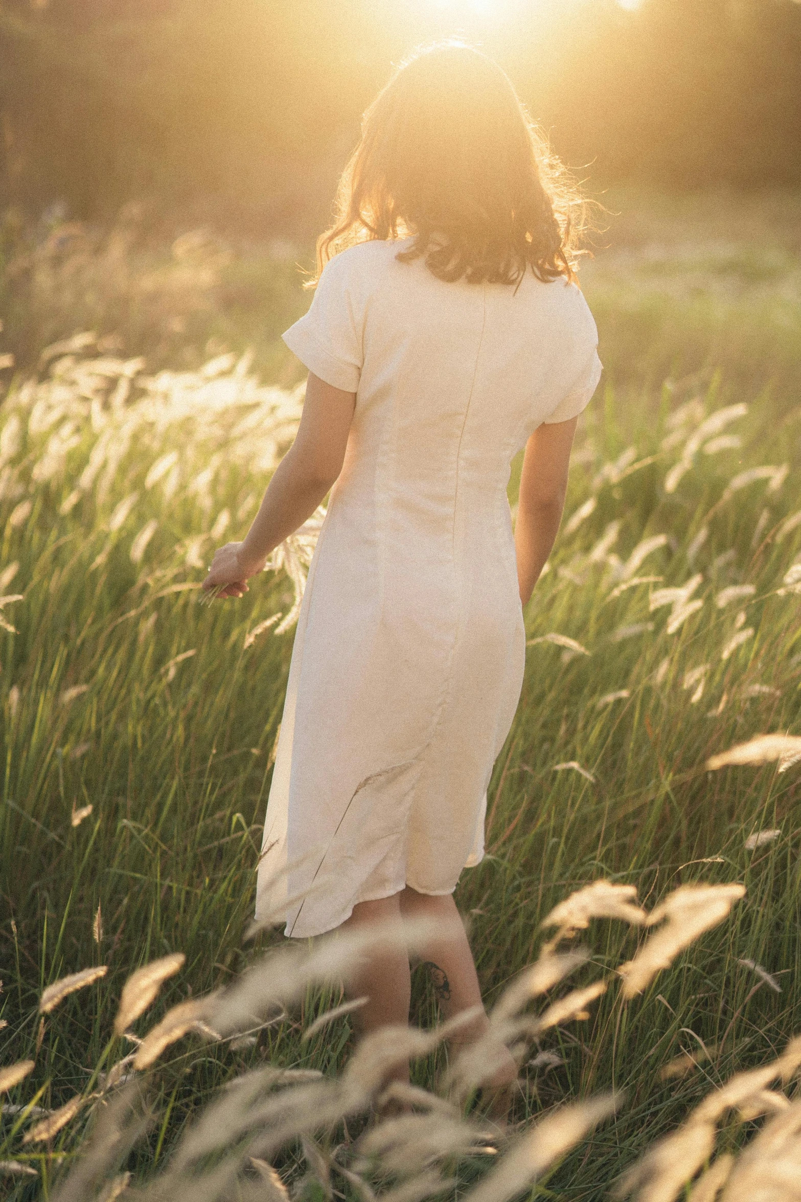 a woman in a white dress is walking through the tall grass