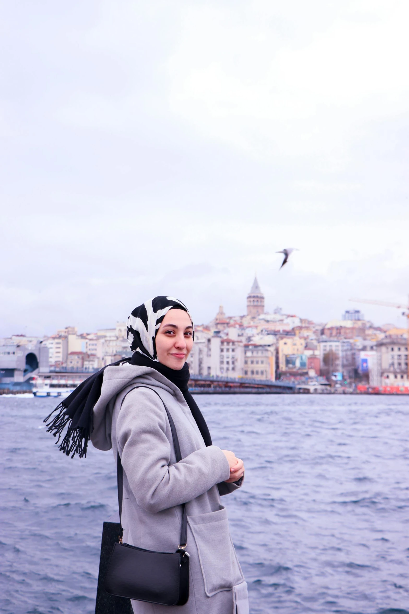 a woman poses on a pier with a city behind her