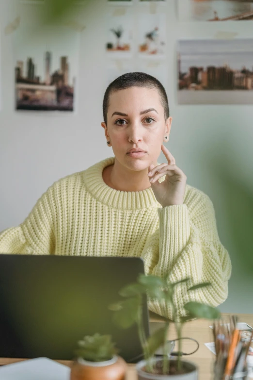 a woman is sitting at a laptop with her hand on her cheek