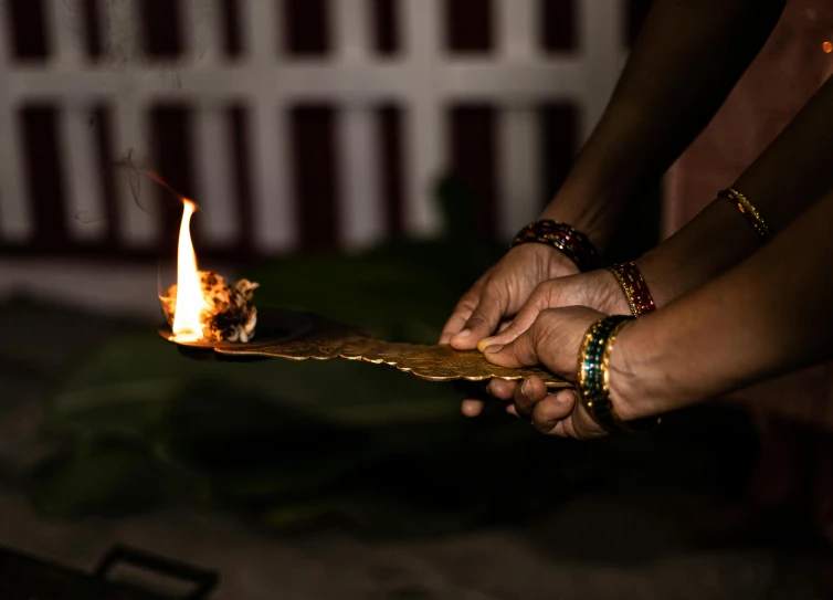 two hands holding out a piece of wood that is burned in flames