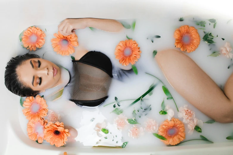 a woman is laying down in a bath with orange flowers