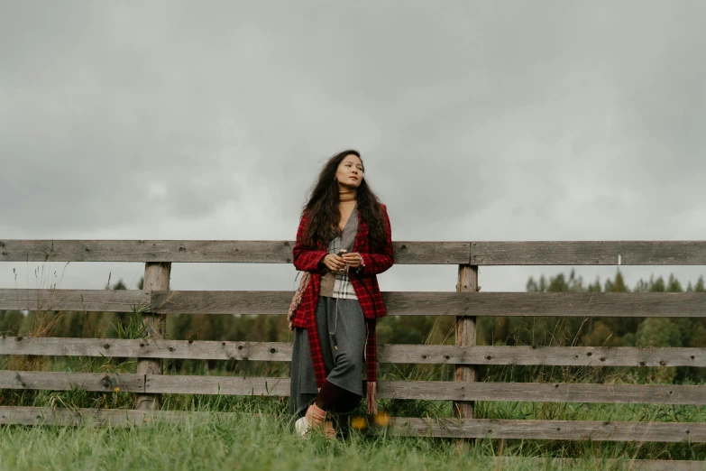 a woman in a dress leaning against a fence