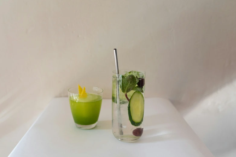 a green drink next to a glass with cucumber in it