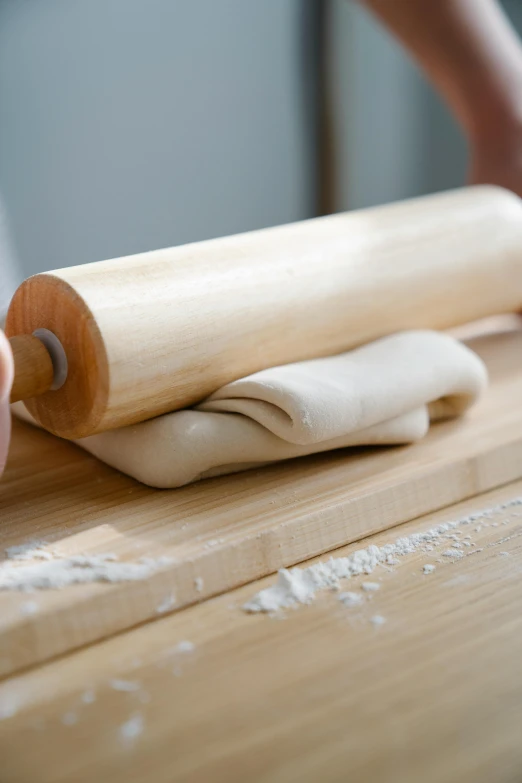 a woman rolling dough onto top of a wooden table