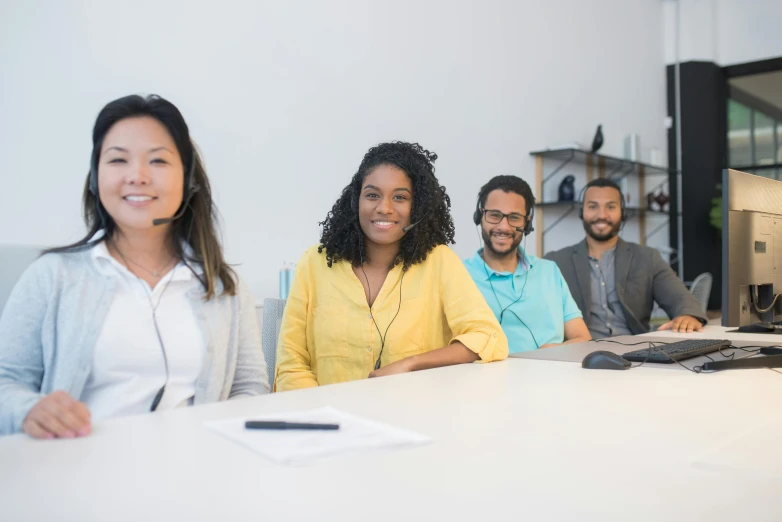 three smiling employees sitting in front of two monitors