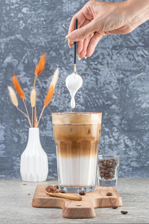 a person spooning sugar onto a beverage in a tall cup