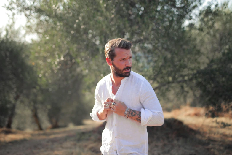 a man standing in a wooded area while adjusting his neck tie