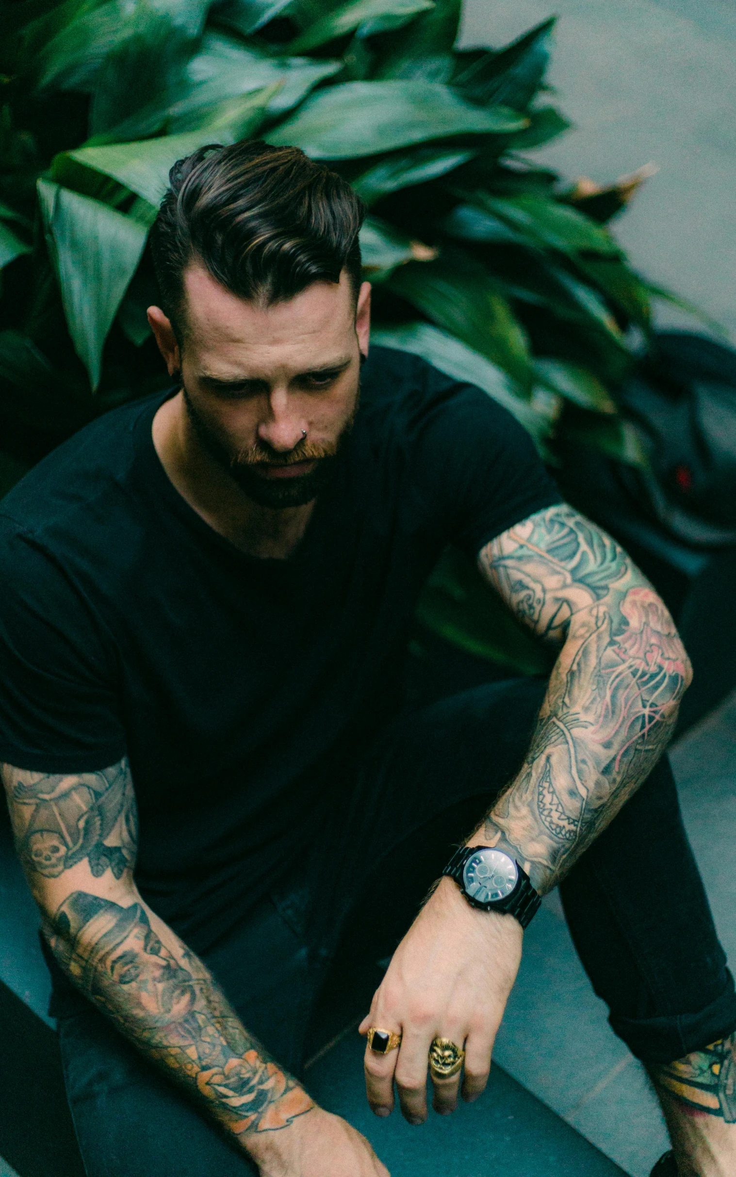 a man with tattoos sits down and is looking at his watch