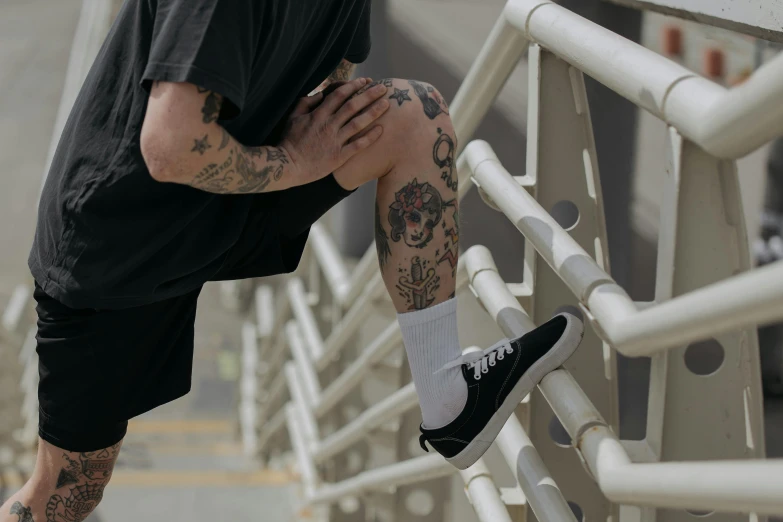 a person in black shirt and shorts standing near rail with arm and foot tattoo