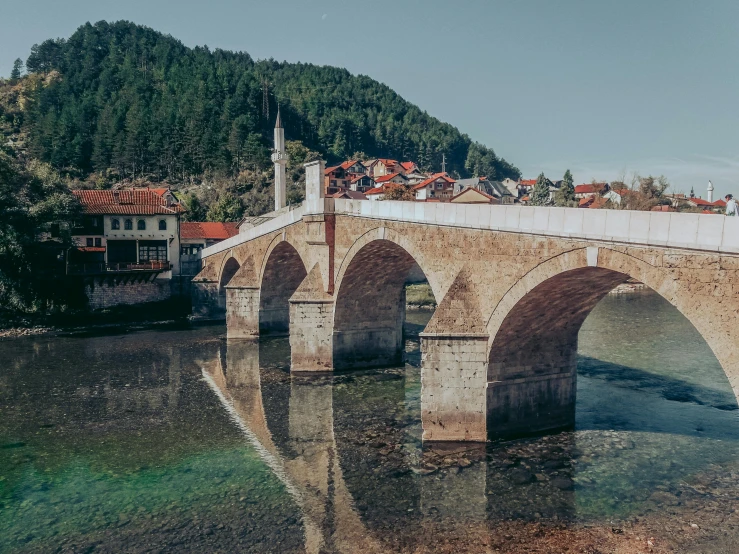 bridge surrounded by mountains and buildings in front of lake