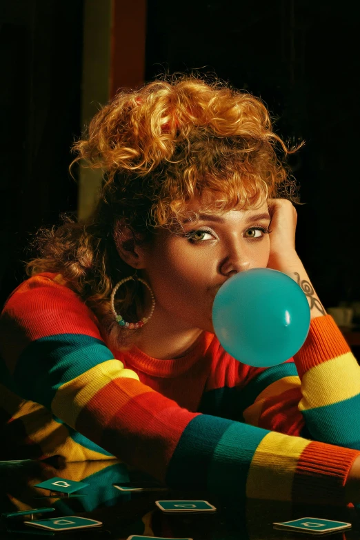 woman with curly hair blowing a bubble of blue, yellow and red