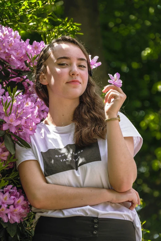 young woman in striped shirt holding purple flower while standing outdoors