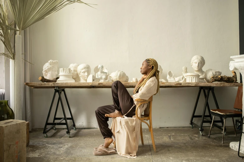 a person sitting on a chair in front of a table with white marble head sculptures