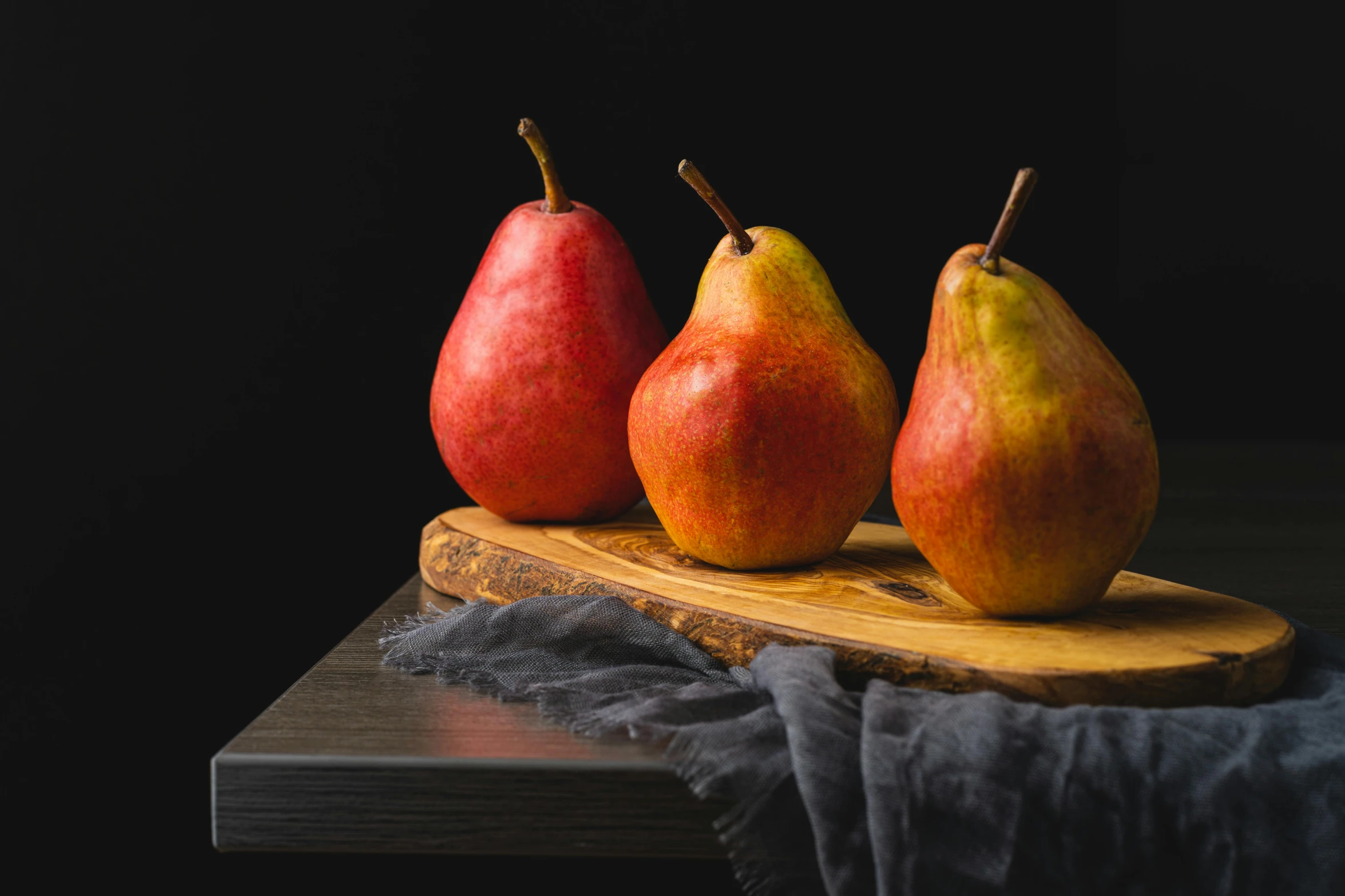 three pears sitting on a wooden plate next to each other