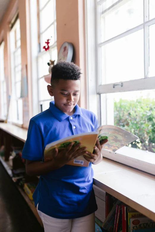 a  standing in front of a window holding a book