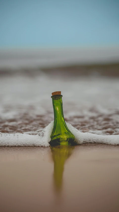 a bottle of wine sitting on a beach in the sand