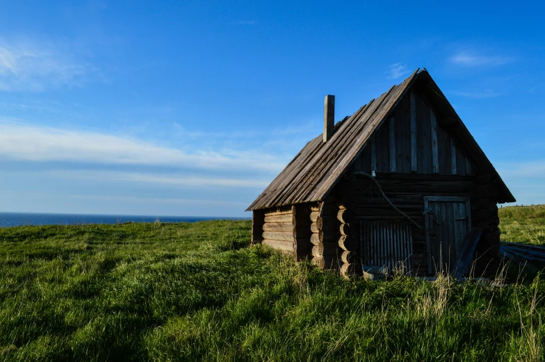 small log house with door and windows on grassy hill