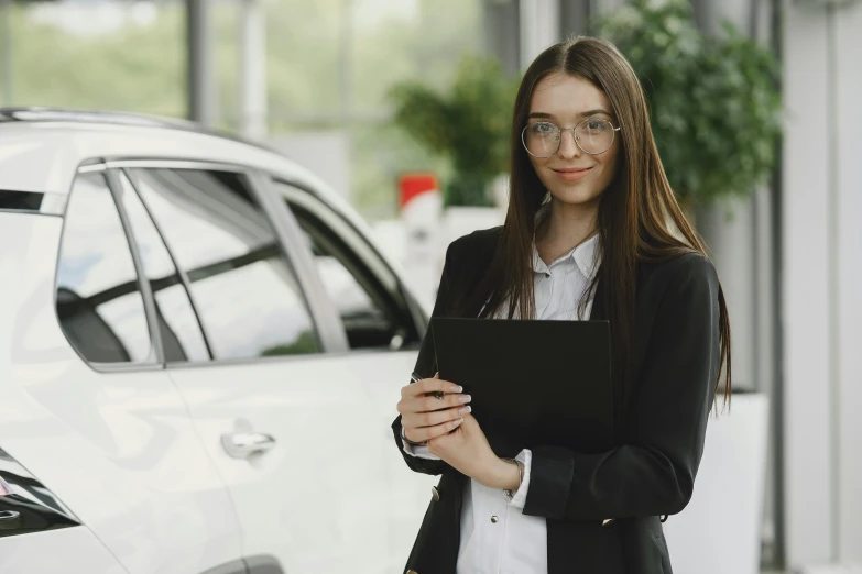 a woman stands next to a parked car holding her clipboard