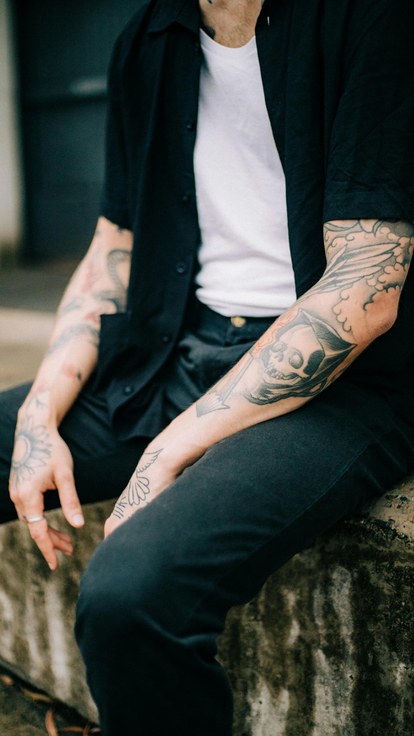 tattooed man sitting on a brick wall and smoking a cigarette