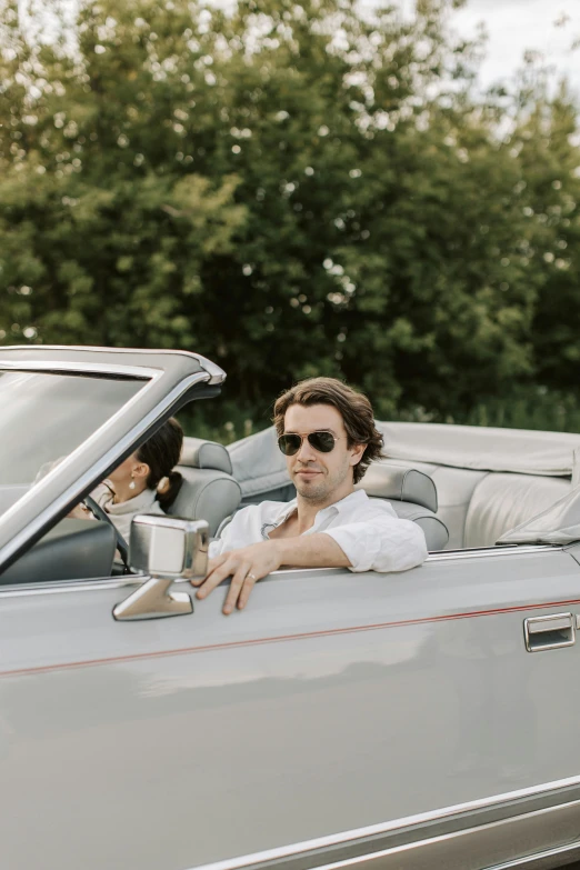 a woman standing behind the door of a car and looking out into the street while a man sits inside it