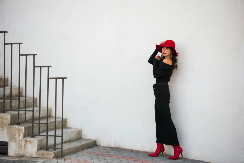 a woman wearing red hat leaning against wall with stairs behind her