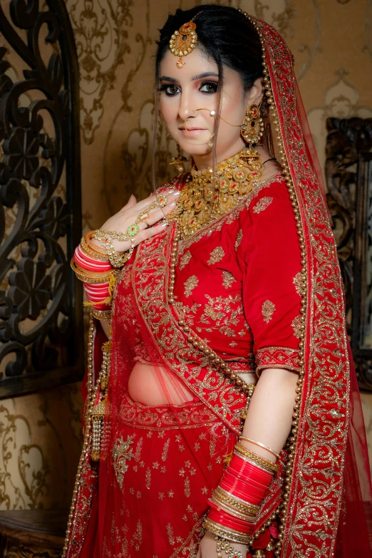 a bride with a very dark hair and bright makeup stands in a red traditional indian wedding dress