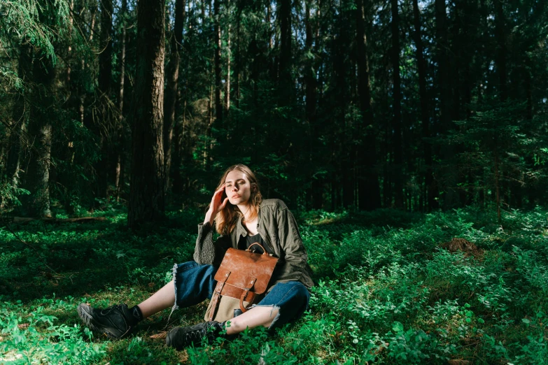 a young woman in a coat sitting on a forest floor