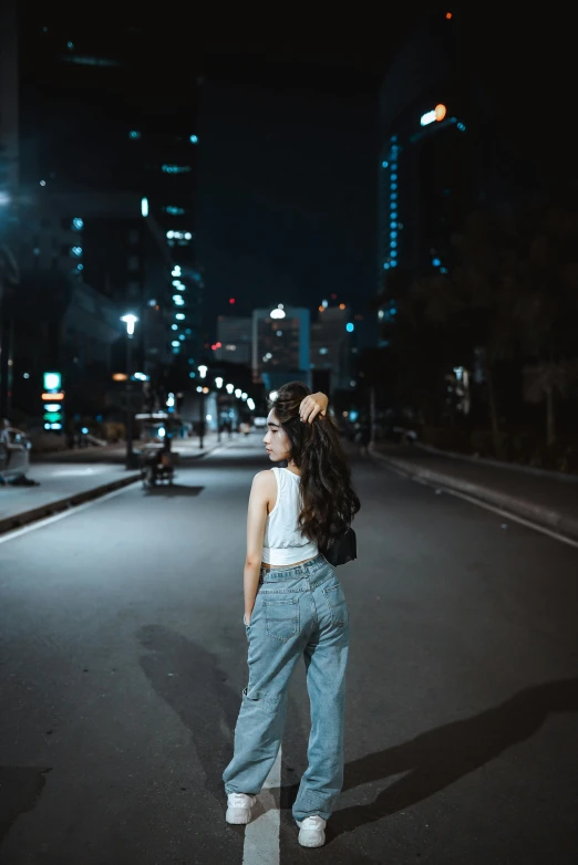 woman wearing jean pants and hat standing on city street at night