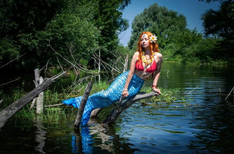 a woman with long red hair sitting on top of a log in the water