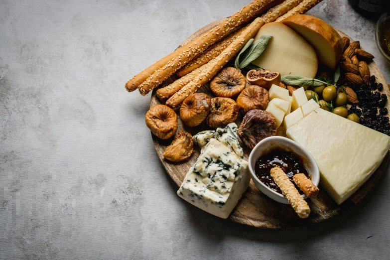 various cheeses, bread sticks and nuts are on a wooden plate