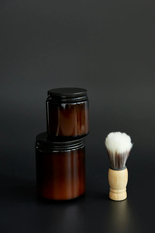 a brush next to a glass container with a brown handle