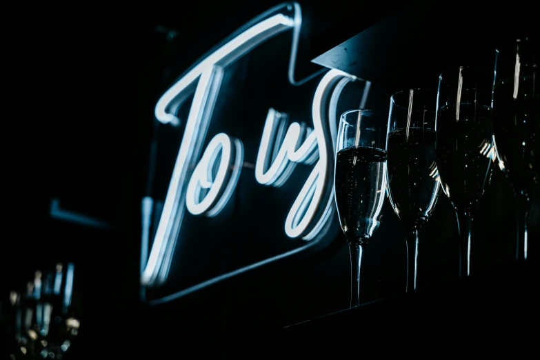 a neon sign has glasses filled with champagne