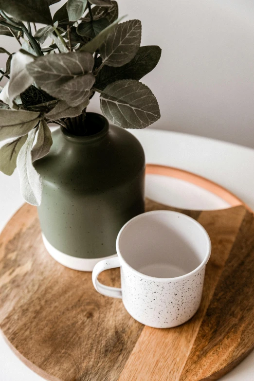 the small cup and vase sit next to each other on a round wood tray