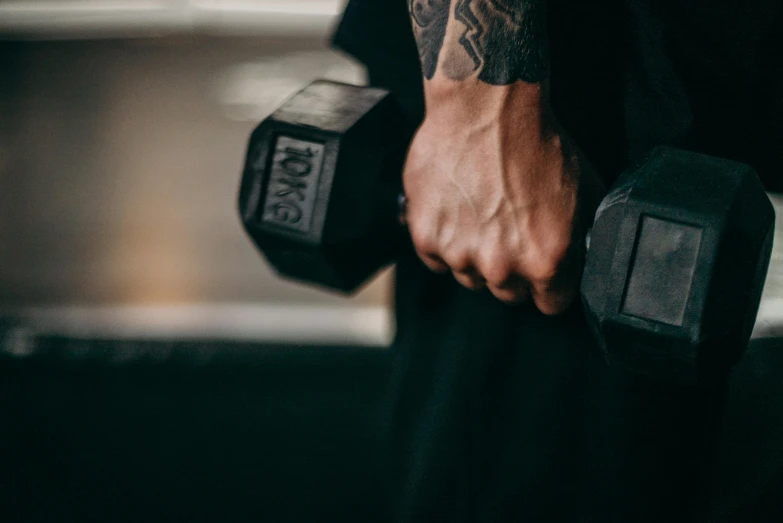 man in tights with tattooed arm holding two dumbbells