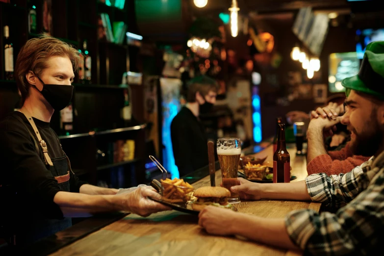 three people wearing face masks eat food at a bar