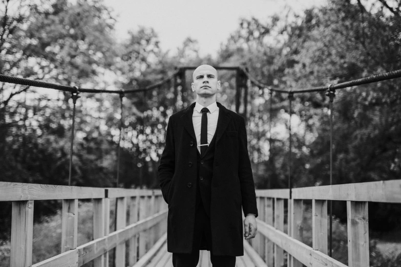 a man with sunglasses and a coat posing for a po on a wooden bridge