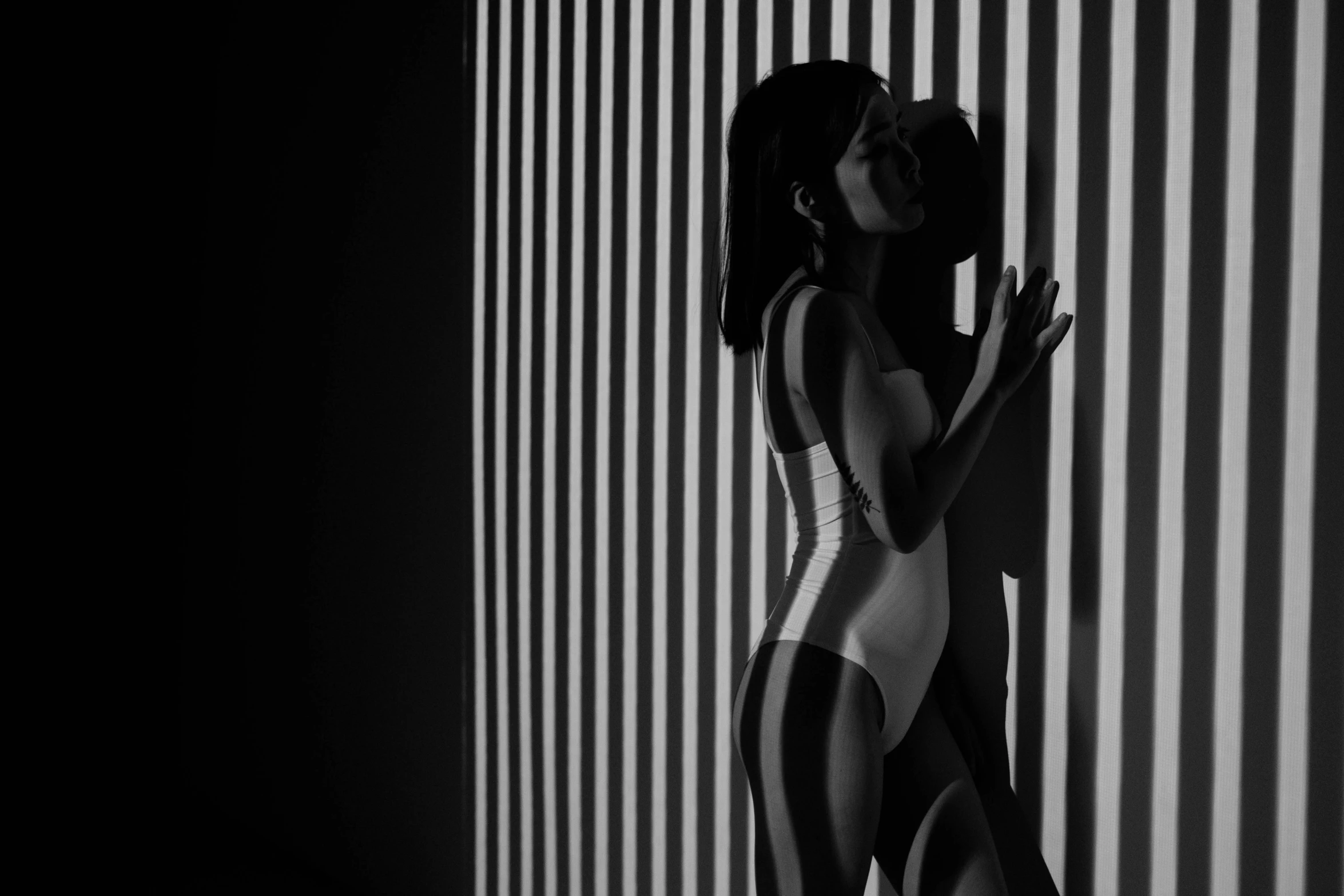 a woman in a bodysuit stands with her arm on a striped wall