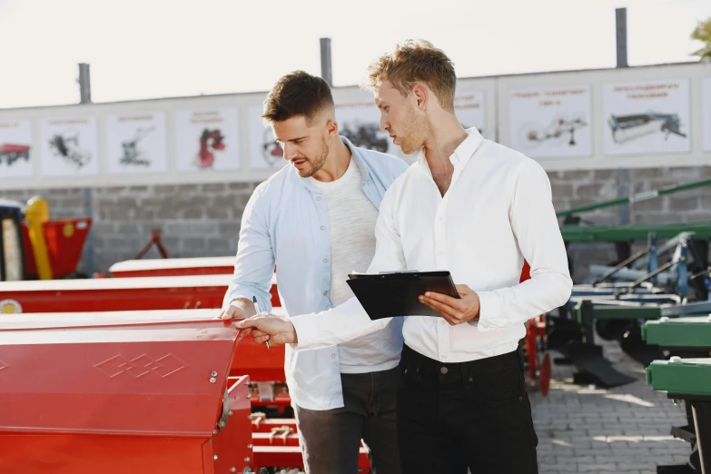 two men are standing by two red machinery