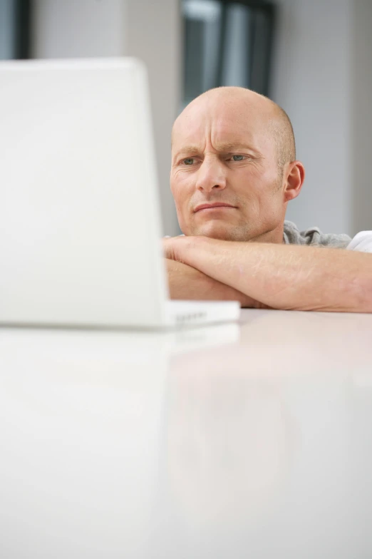 a bald headed man sits at a table while on his laptop