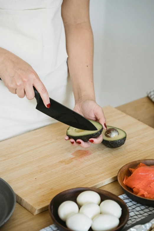 a person holding a knife to cut an avocado