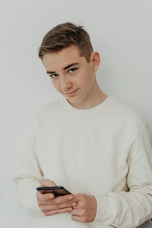 the young man is using his cellphone while wearing a white sweater