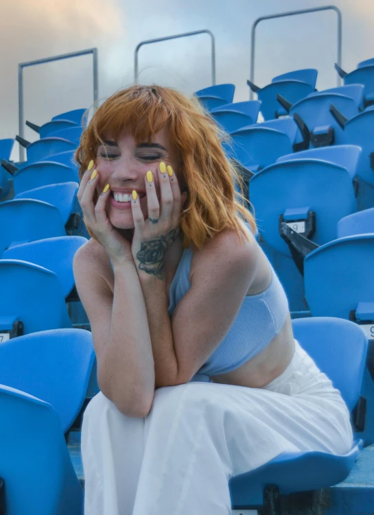 a  with red hair is sitting on a blue stadium bench